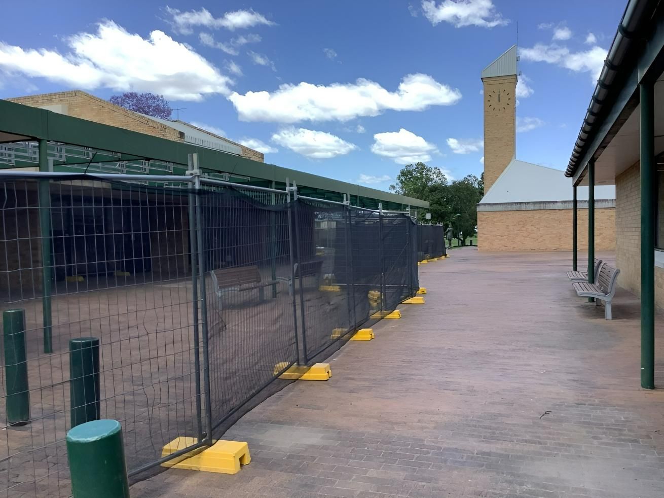 A Fence Is Surrounding a Brick Building with A Tower in The Background — Site Safety NSW in Sandgate, NSW