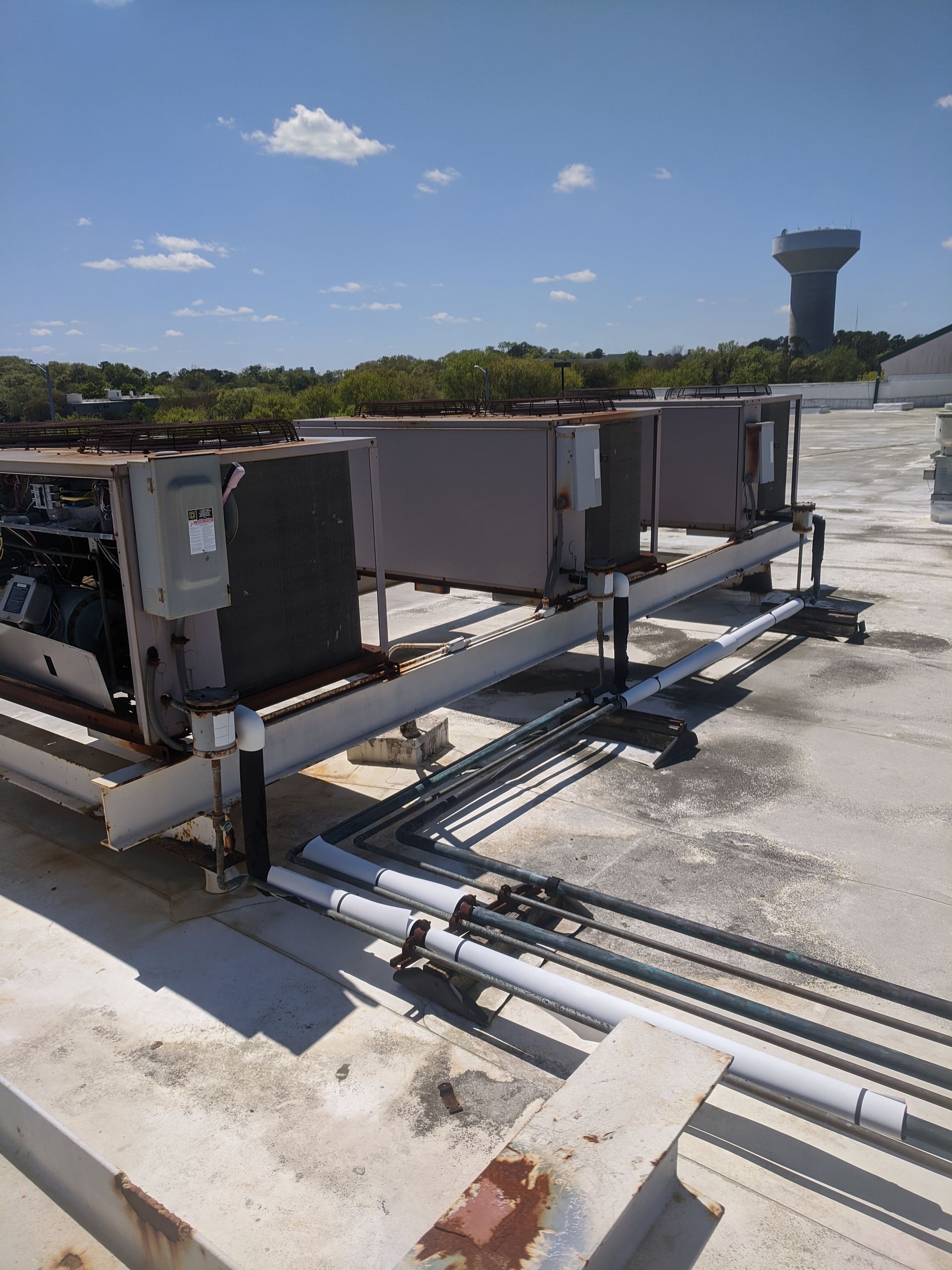 Rooftop HVAC units with electrical boxes and piping, set against a blue sky and water tower backdrop.