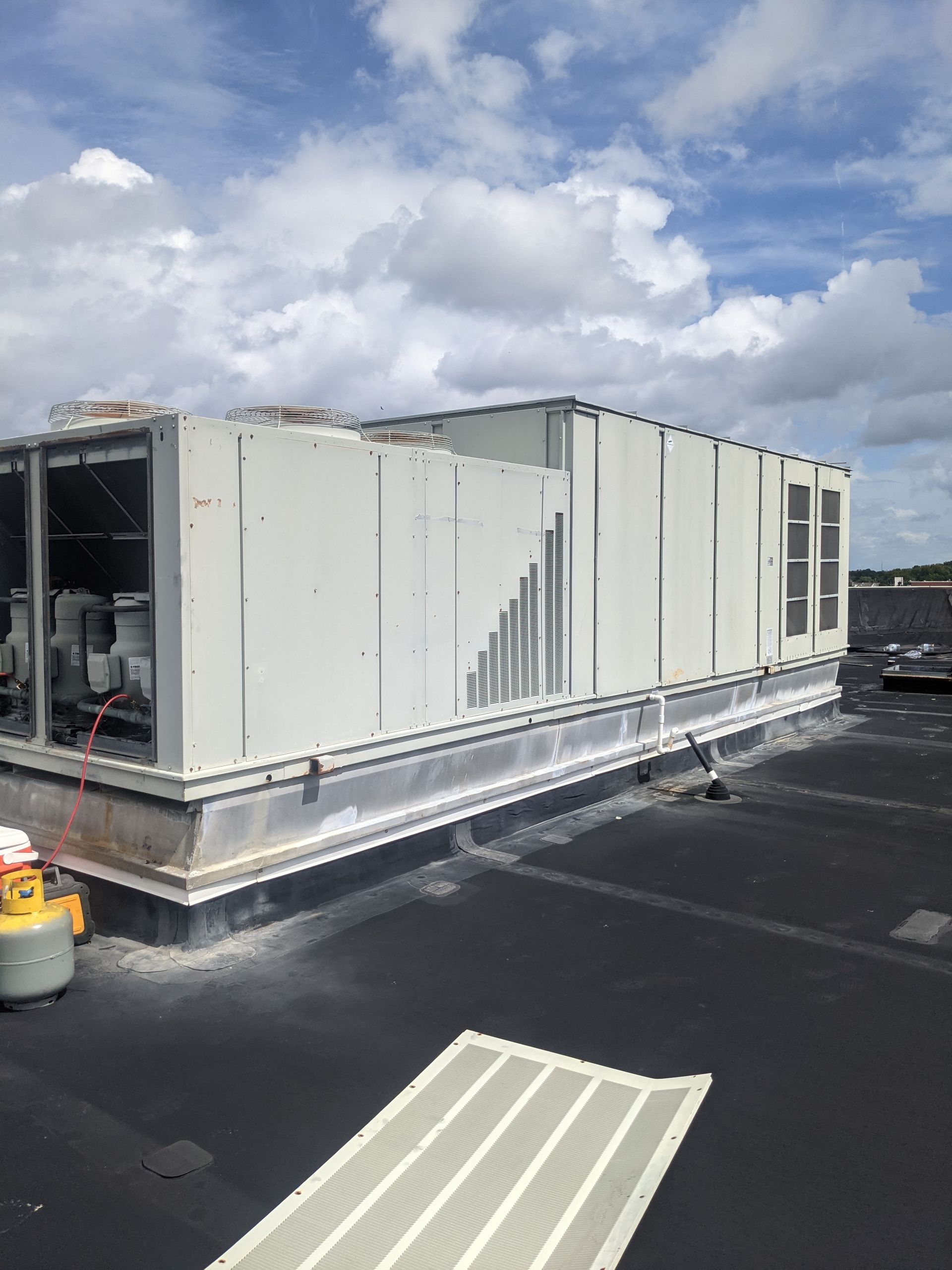 Commercial Packaged Rooftop Unit Repair HVAC unit on a flat rooftop under a cloudy sky. The unit is white/gray, and the roof is black.
