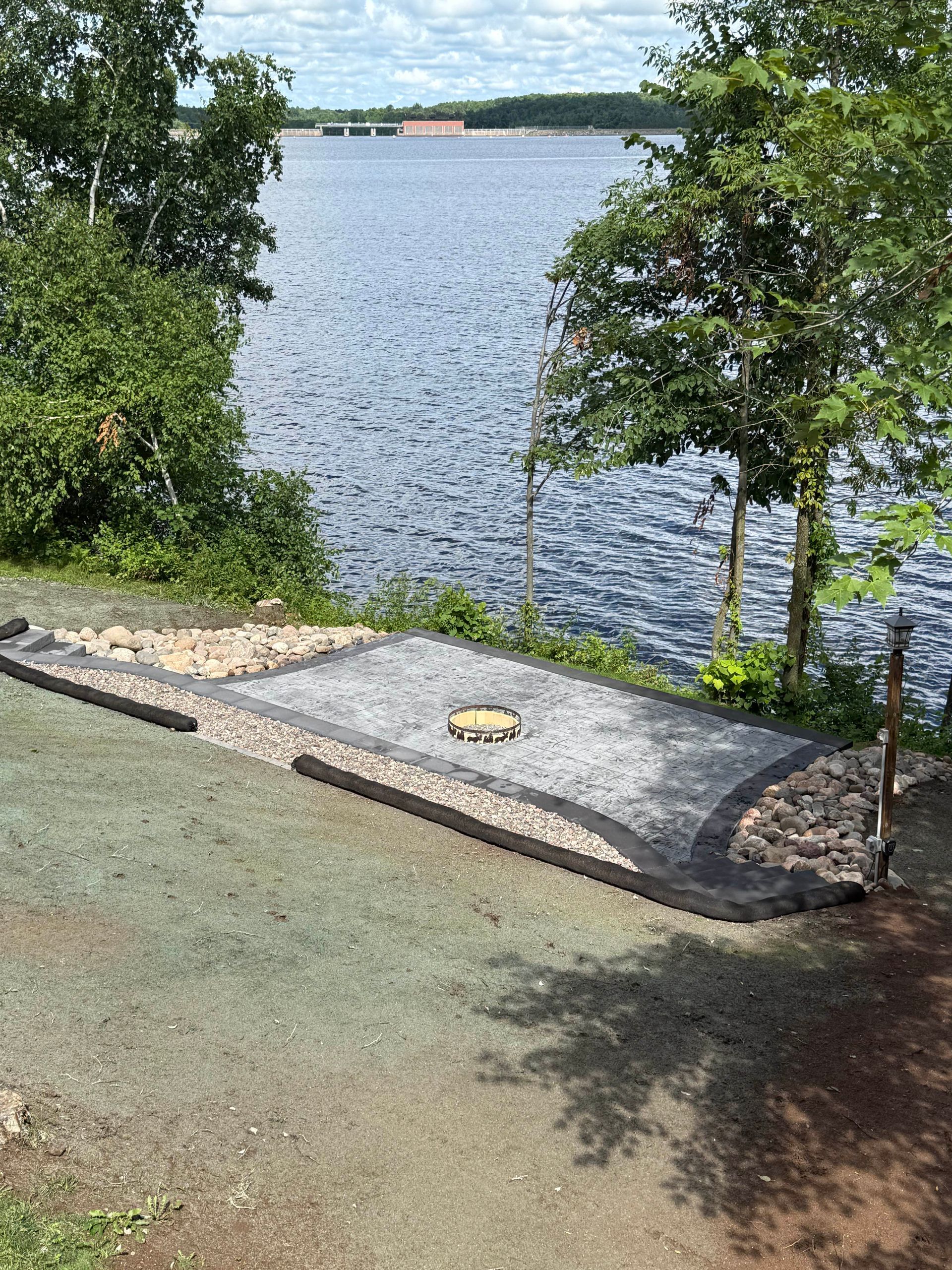 Gravel launch ramp beside a calm lake, framed by green trees on a sunny day.