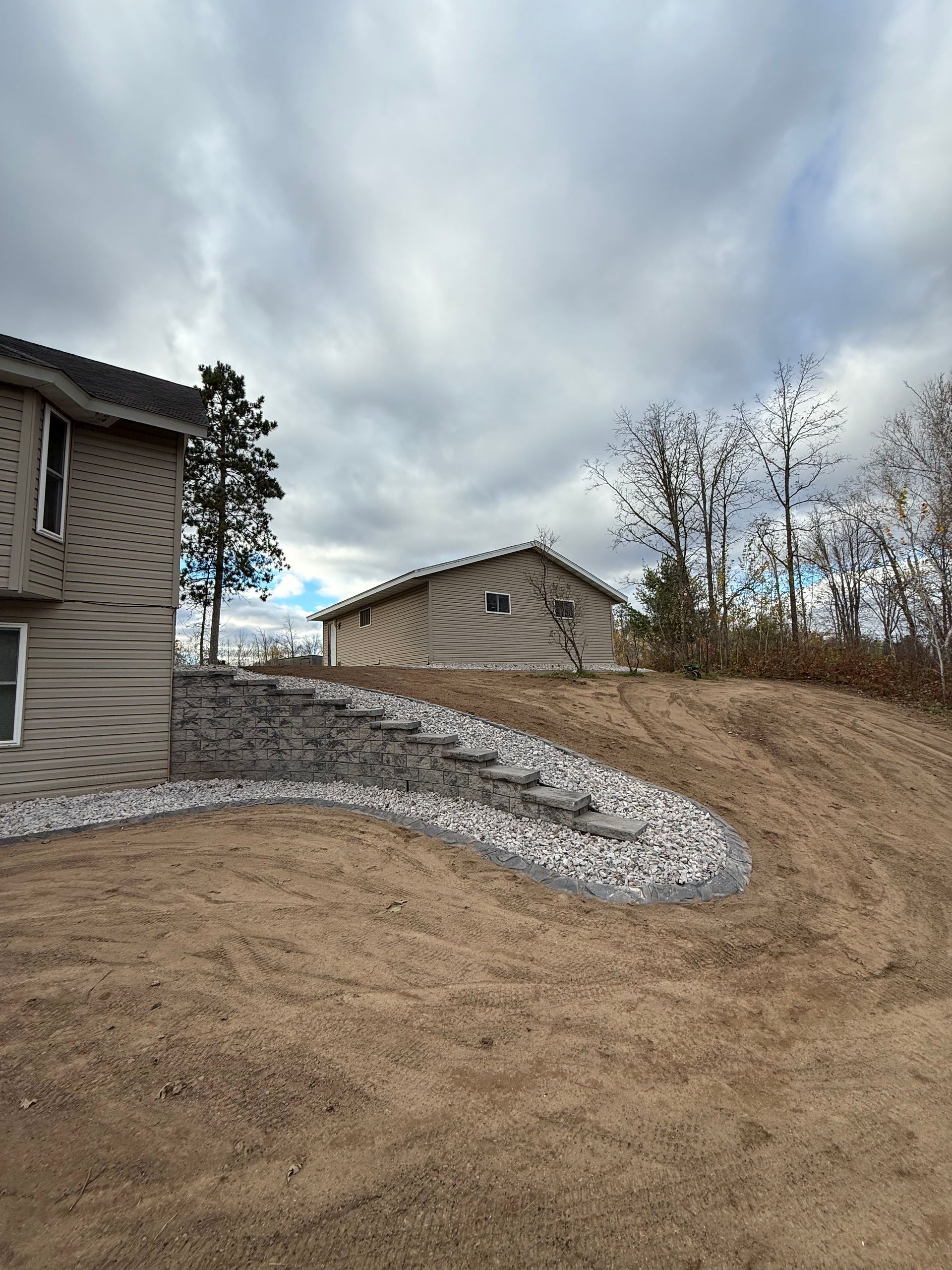 Residential yard with tan grass, stone retaining wall, and cloudy sky