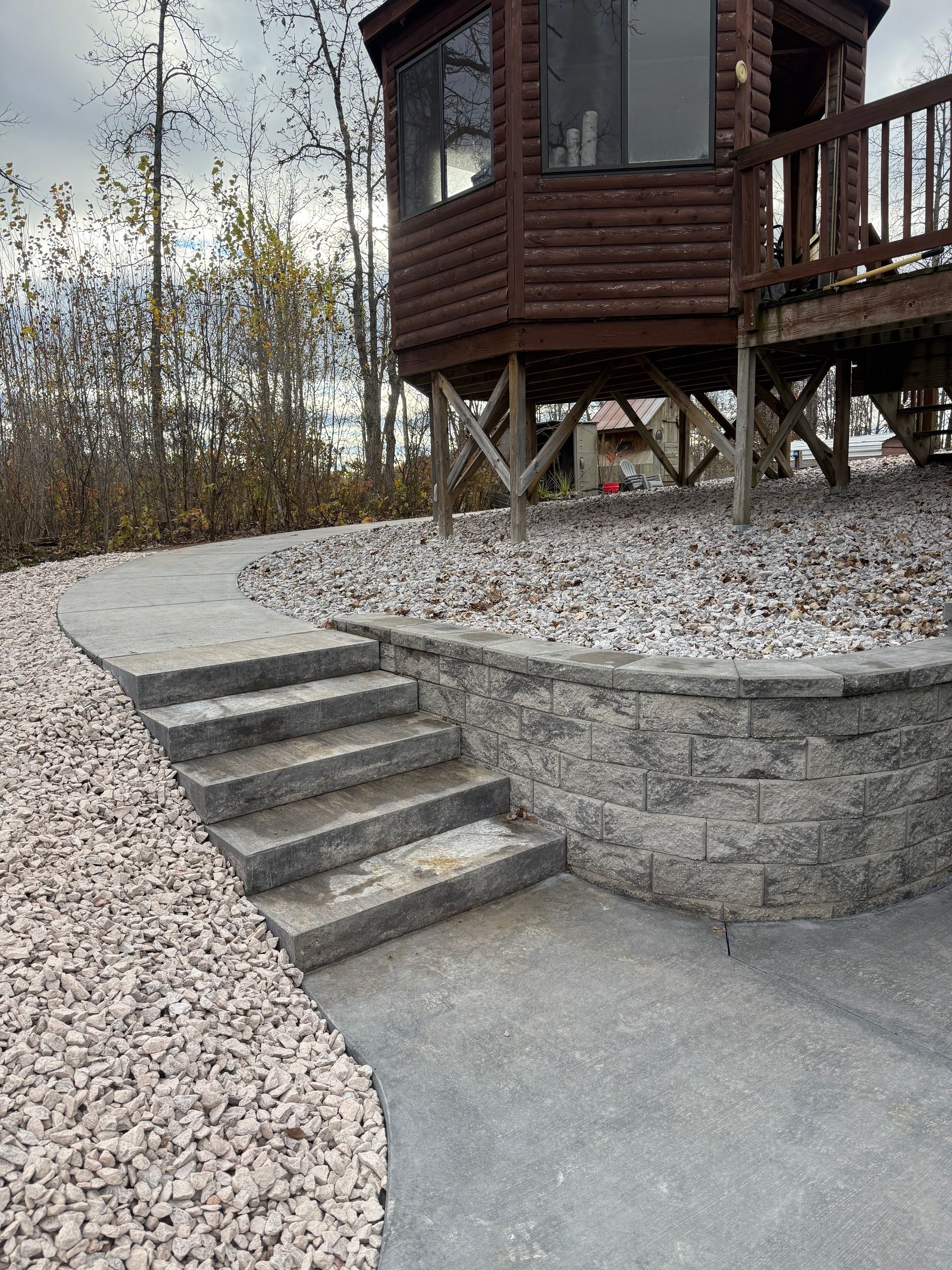 Gravel path with concrete steps leading to a wooden lookout cabin on a raised stone base.