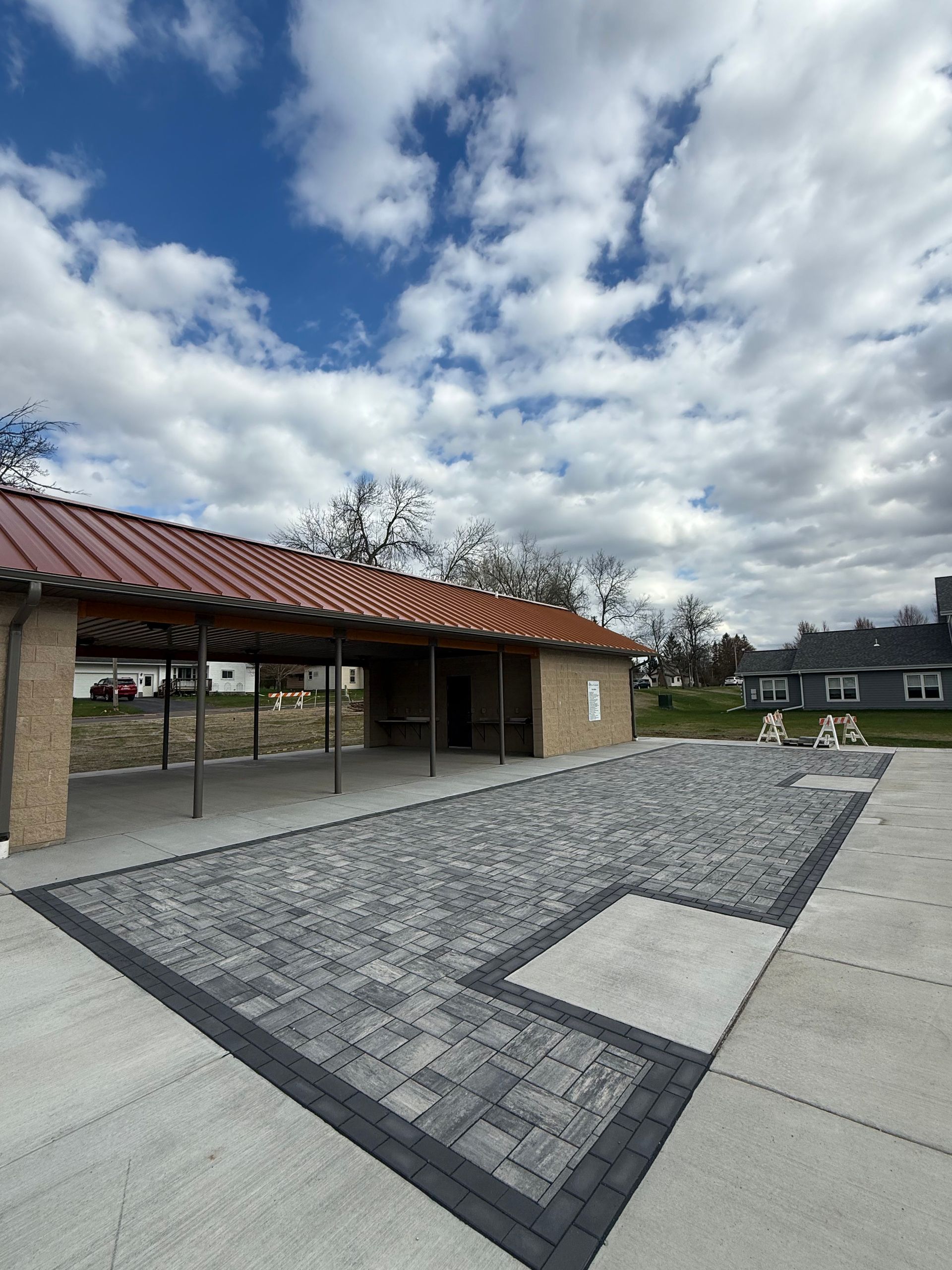 Covered brick patio with red roof, gray pavers, and cloudy sky in a courtyard setting