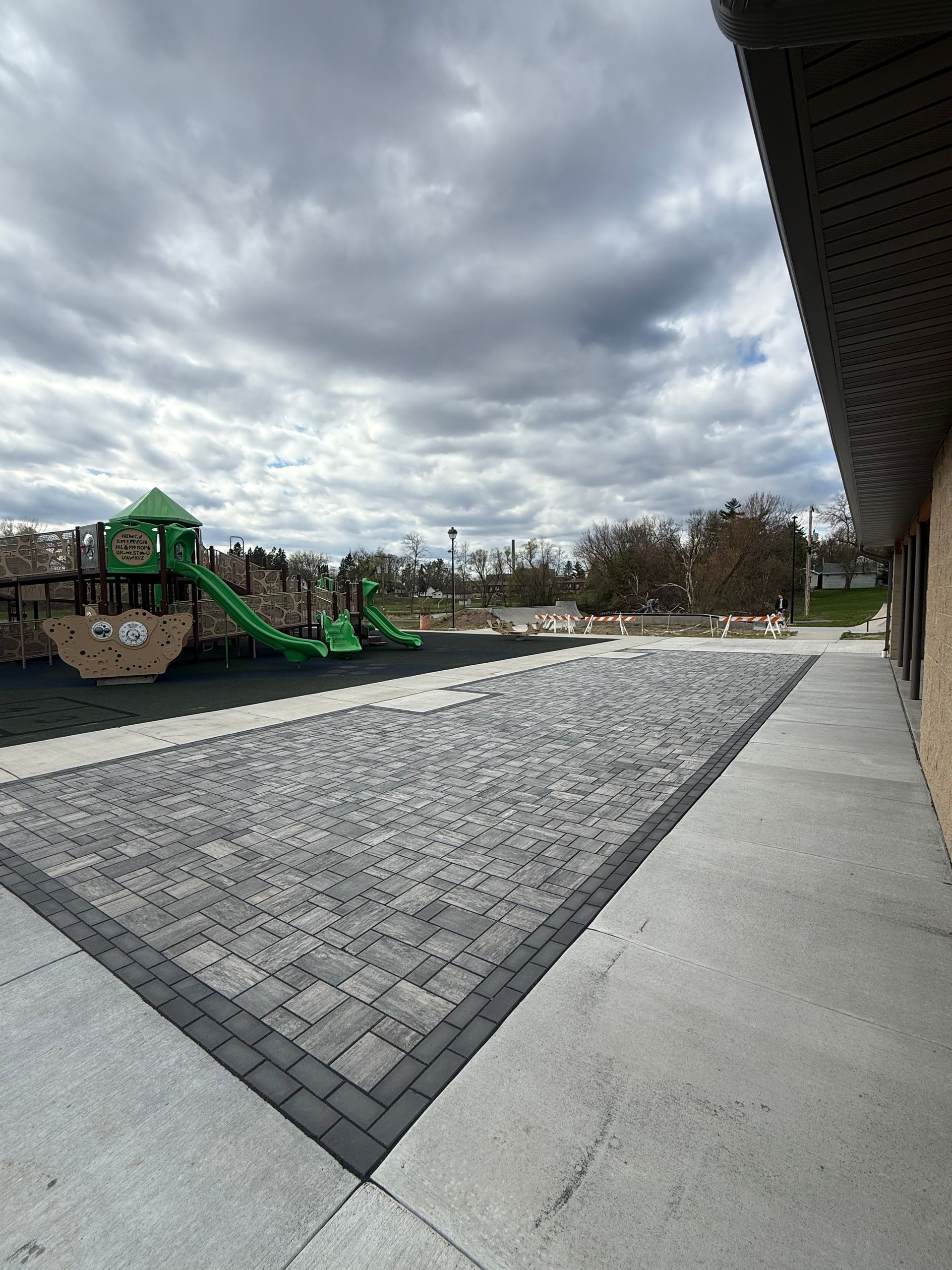 Gray paver courtyard with green playground equipment under a cloudy sky