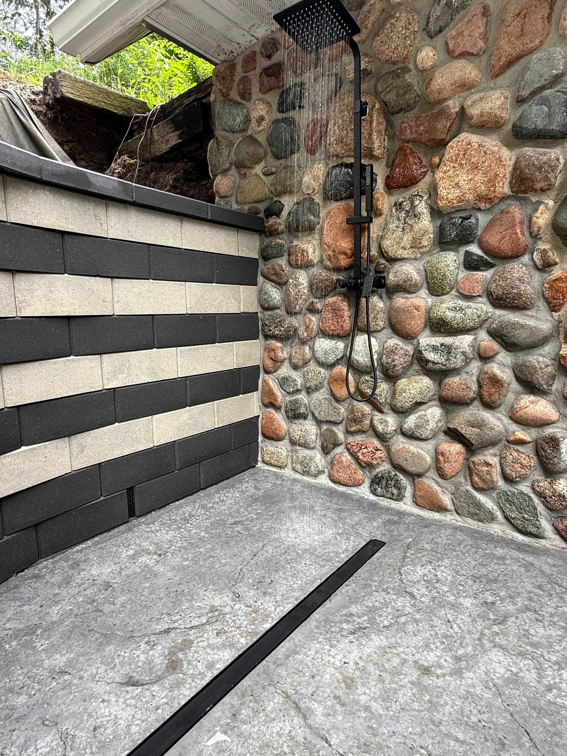 Stone and striped wall corner with a small waterfall, concrete patio, and drainage channel