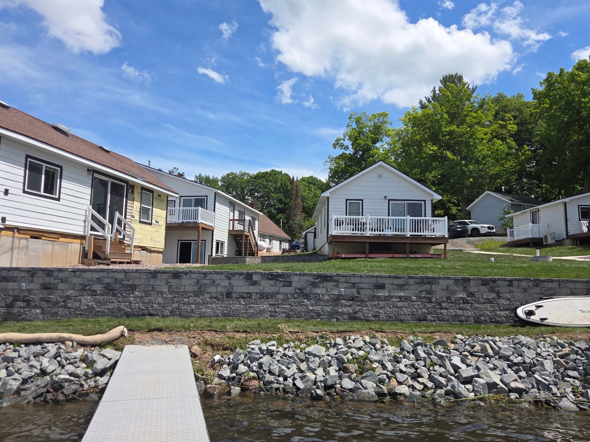 Waterfront houses with a stone seawall and a wooden dock under a partly cloudy sky