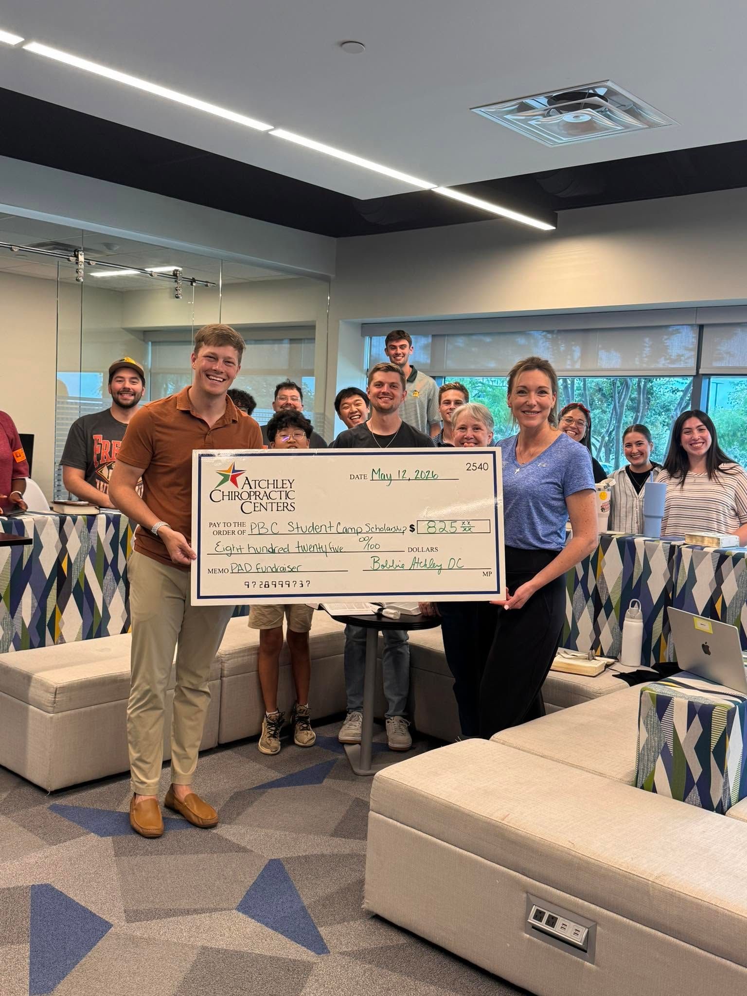 Group of people in a modern office holding a large check and posing for a photo