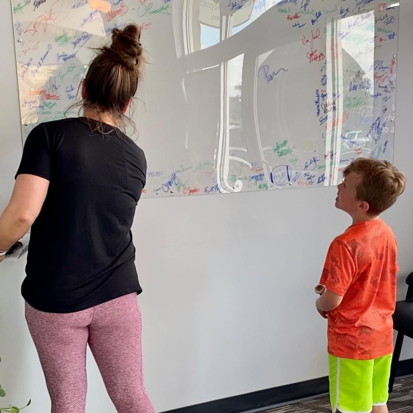 Adult and child writing on a whiteboard covered in marker notes and drawings