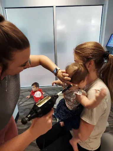 Hairdresser styling a child's hair while another child sits nearby in a salon chair
