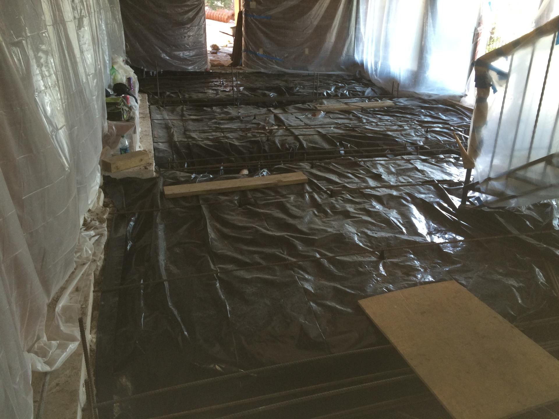 Interior view of a construction site with black plastic covering the floor, rebar, and temporary wooden supports.