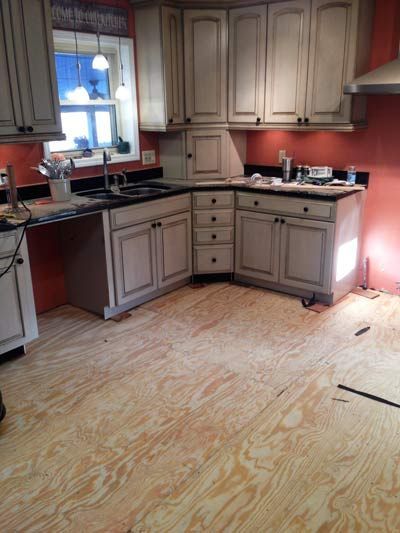 Kitchen with gray cabinets, black countertops, and plywood flooring; a window is visible.