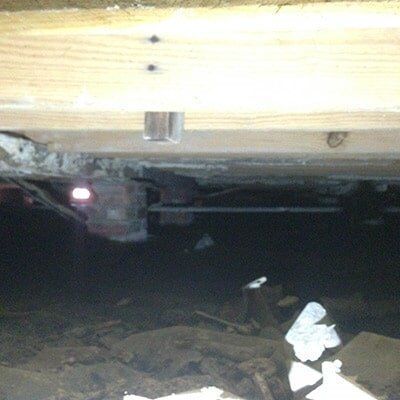 Wooden beam supported by a brick column, viewed in a dark crawl space.