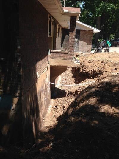Exterior view of house foundation excavation. Earth-toned brick and soil, trench dug along side of the building.