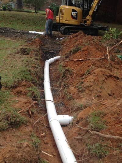 Construction site with white pipes in a trench. A worker and yellow excavator.