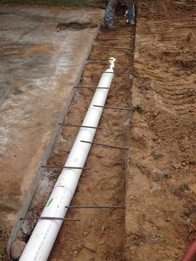 PVC pipe in a trench with rebar, next to concrete, person standing above, dirt surrounding.