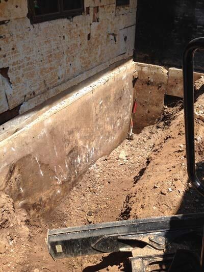 Excavated foundation corner. Soil, concrete wall, and part of a structure.