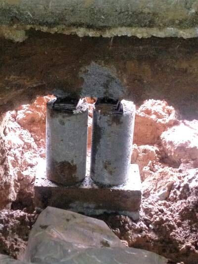 Two weathered cylindrical objects on a brick base, in an excavation.
