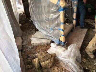 Construction site, concrete slabs on dirt, plastic sheeting. Workers are visible.