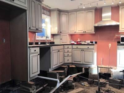 Kitchen renovation. Cabinets elevated. Plumbing and building materials visible. Red wall, gray cabinets.