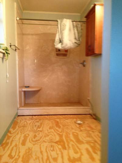 Bathroom interior with plywood floor, shower stall, and wall-mounted cabinet.