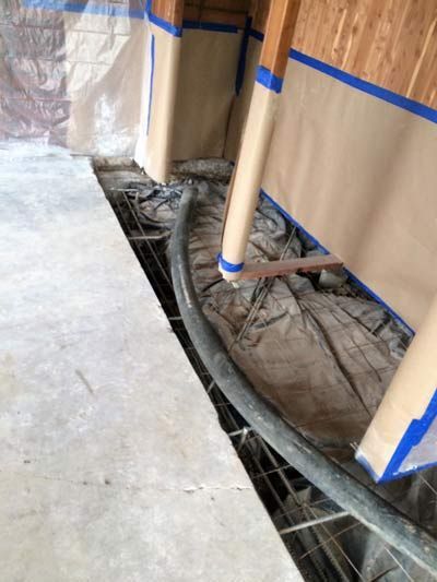 Concrete work in progress; black hose runs through a mesh framework, framed by wood and protected by brown paper.