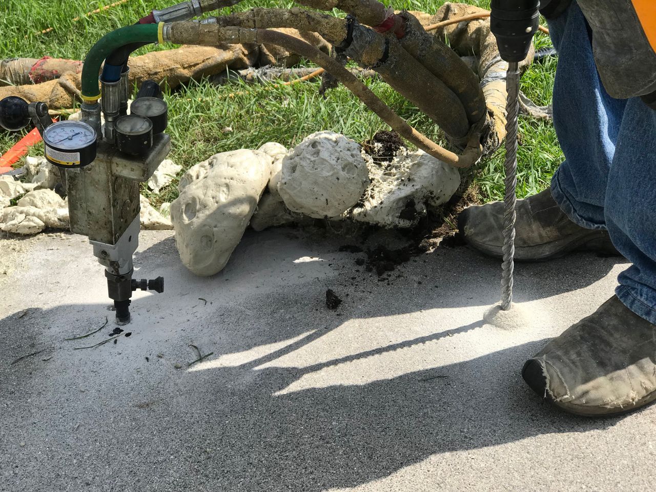 Person drilling concrete with a pneumatic hammer, spraying dust.
