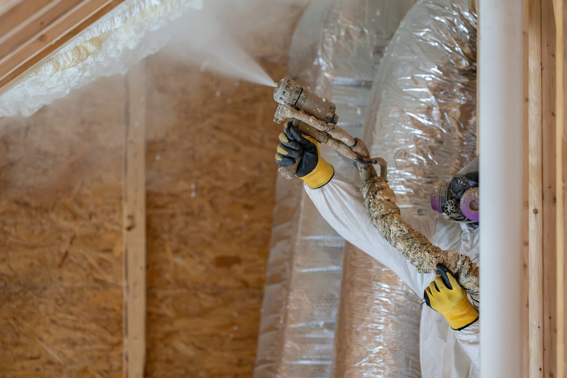 Man in protective suit working under a house with dirt and debris.