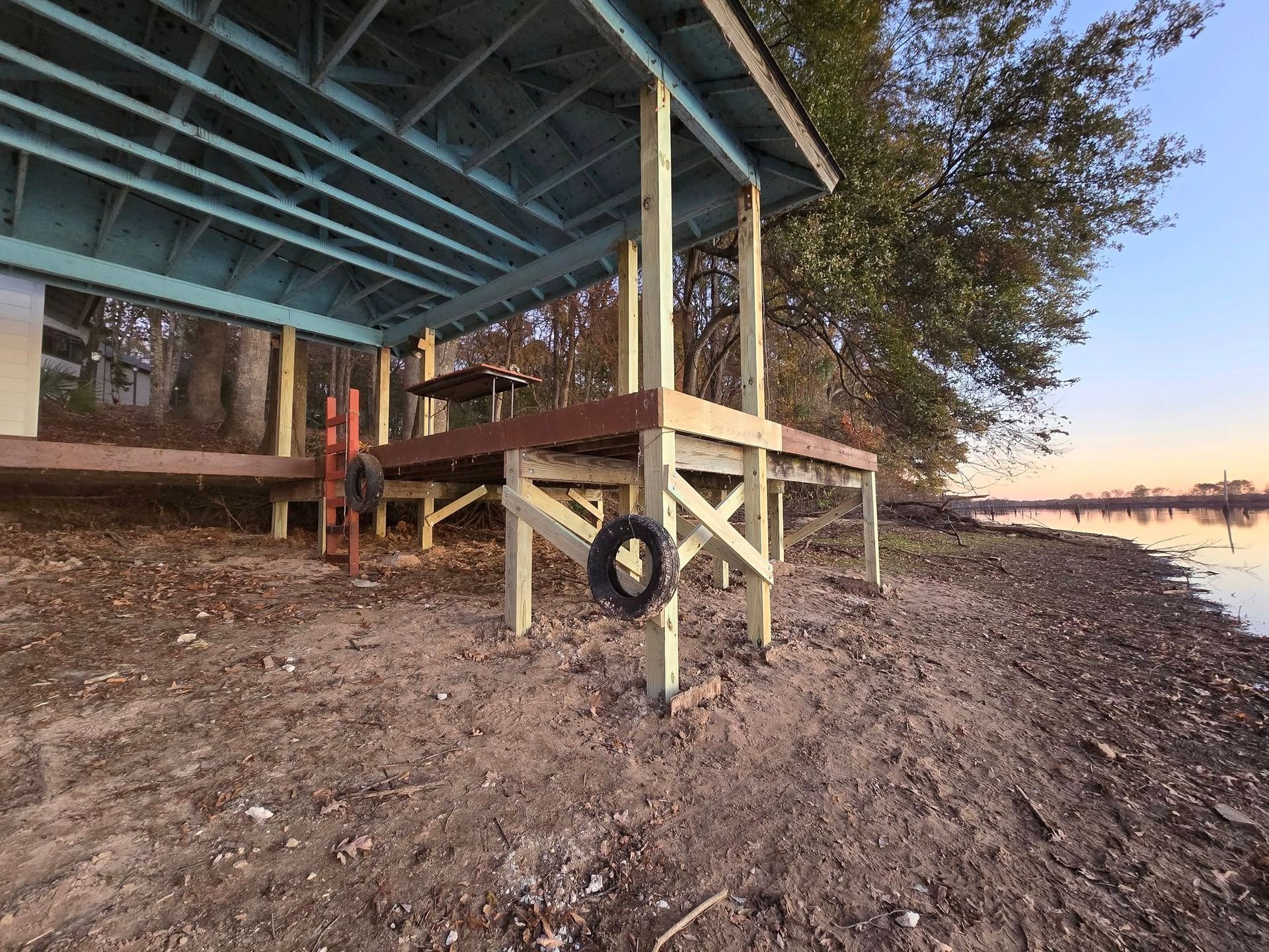 A wooden pier and shelter with a tire swing on a sandy shore by a lake.