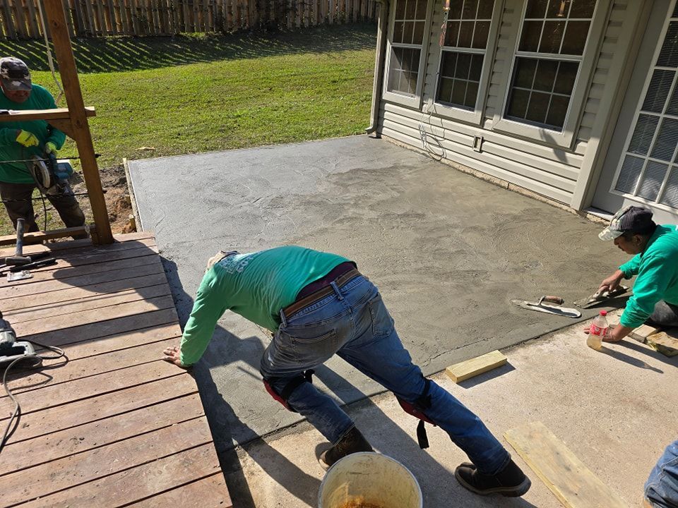 Person installing rebar grid on a dirt patio, next to a house. Green shirt, outside.