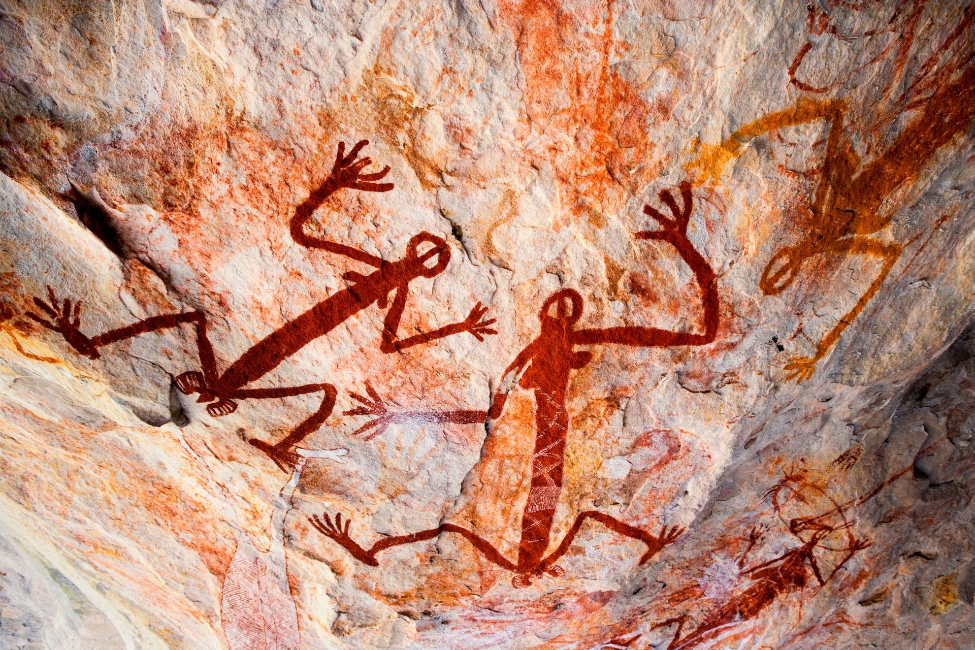 Ancient red cave paintings of human figures on a rocky wall