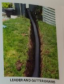 Black drainage pipe in a trench along grass near a building.
