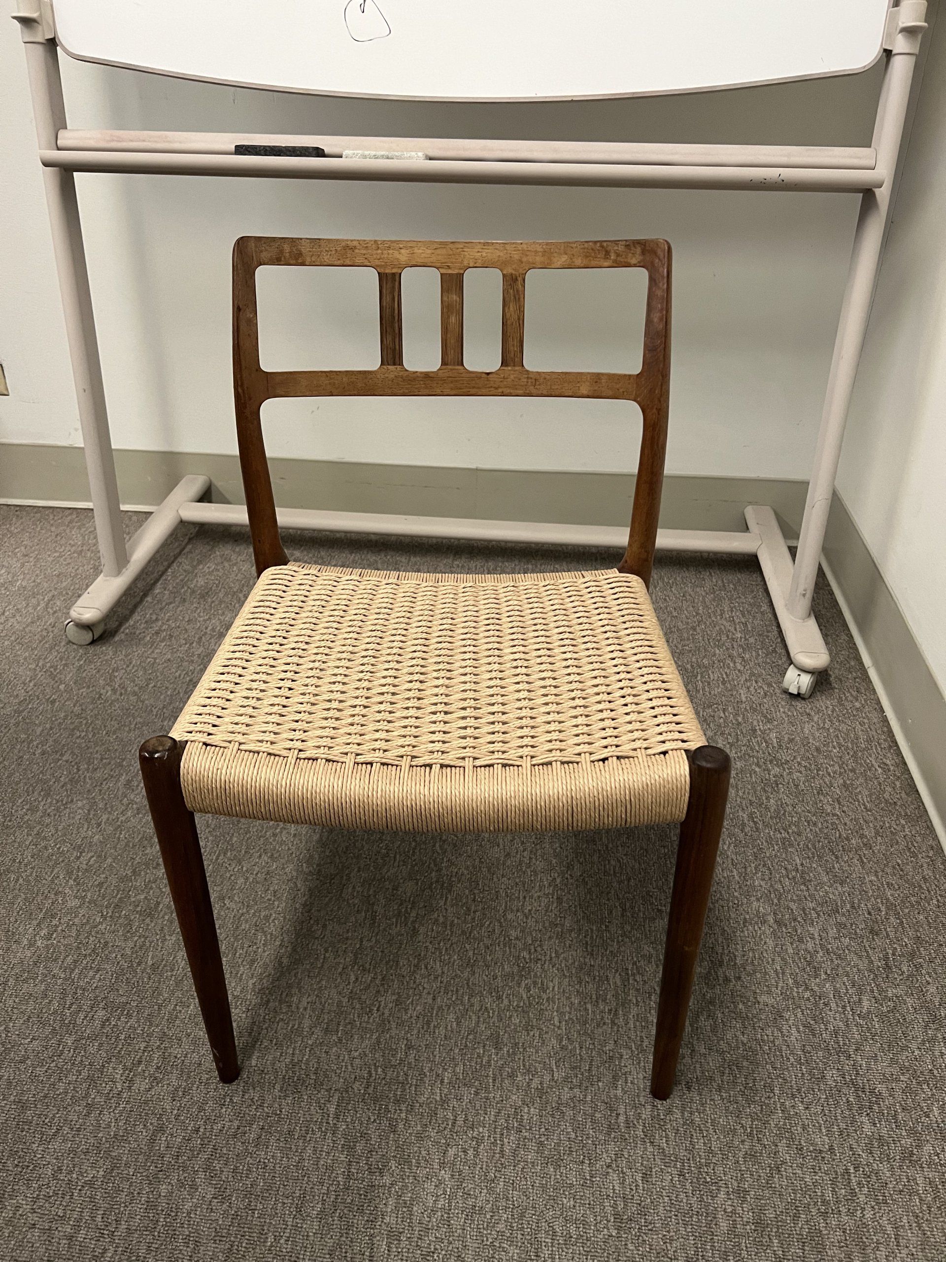 A chair with a wicker seat is sitting in front of a whiteboard.