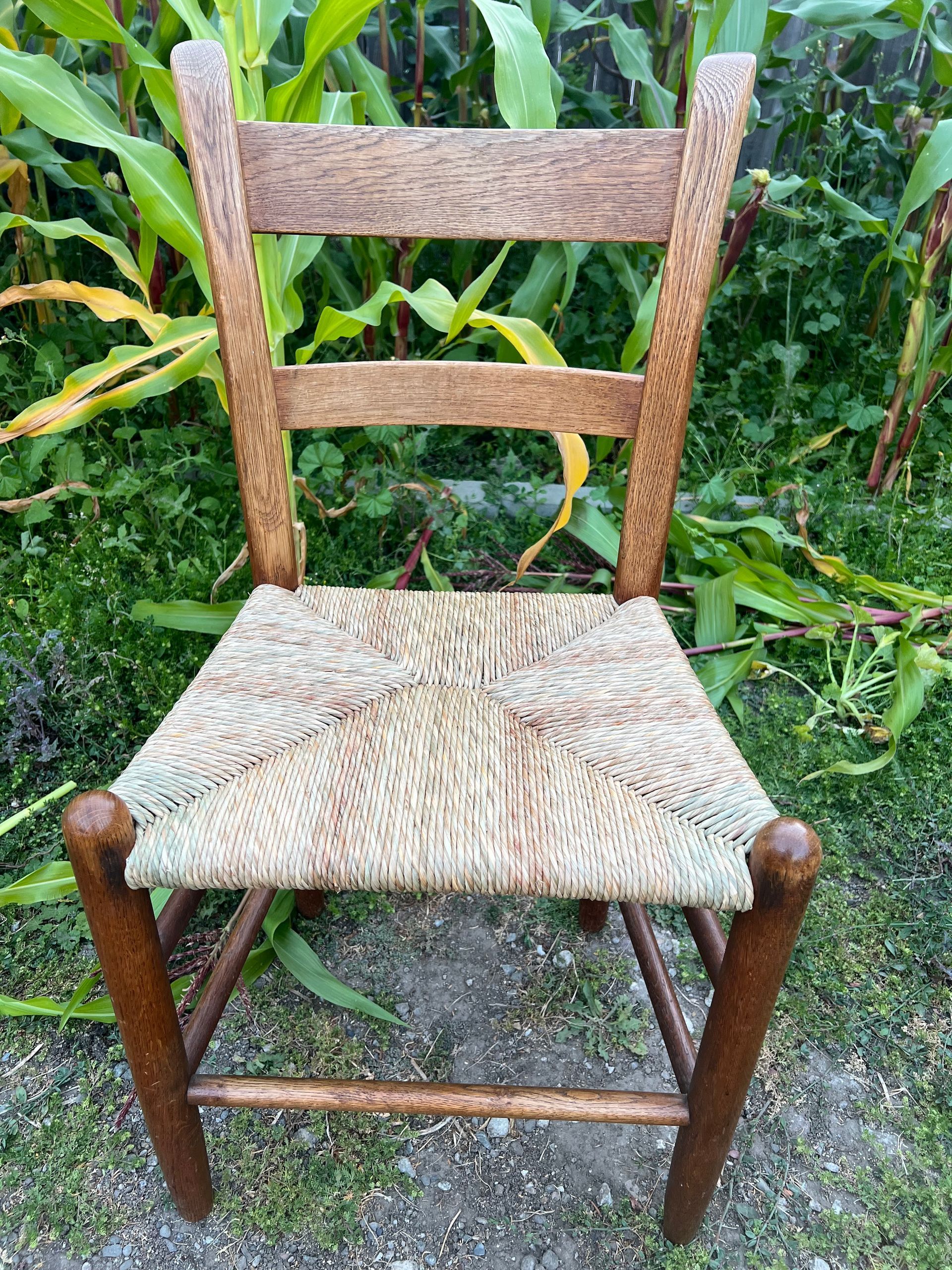 A wooden chair with a woven seat is sitting in the grass.