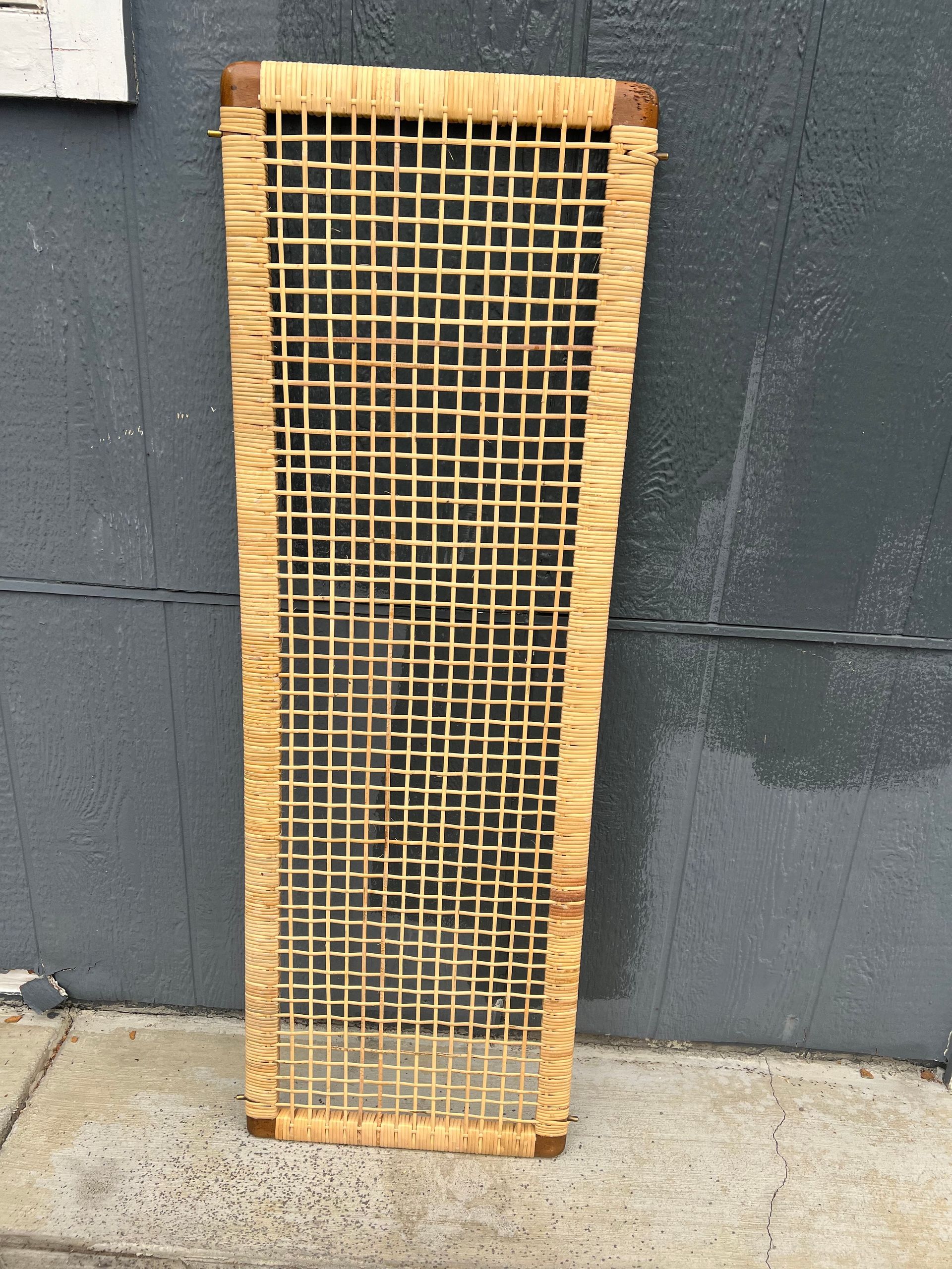 A wicker screen is sitting on a sidewalk in front of a wall.