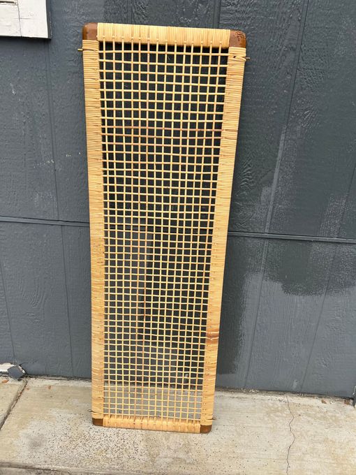 A wicker screen is sitting on a sidewalk in front of a wall.