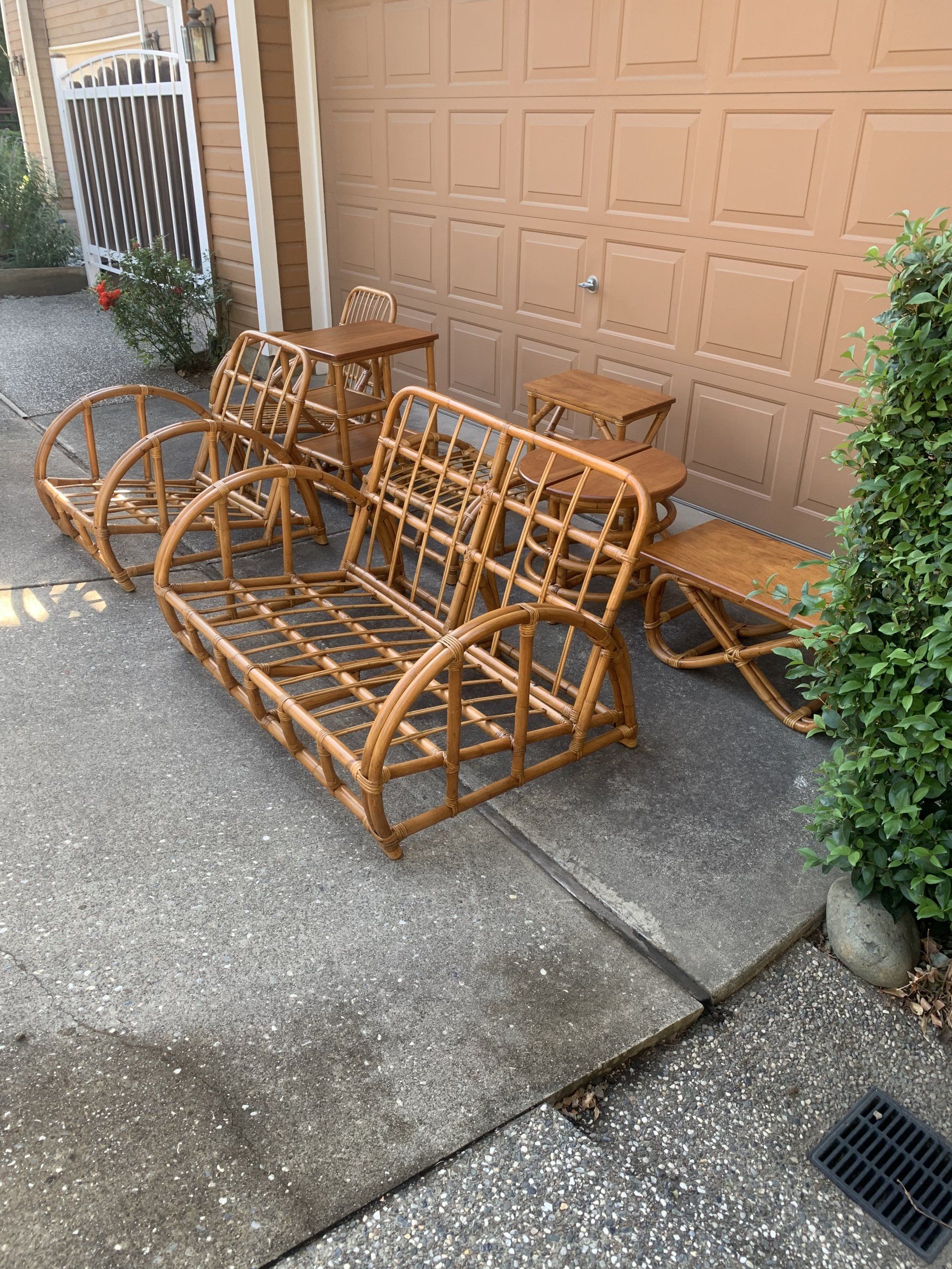 A wicker couch and chairs are sitting on a sidewalk in front of a garage door.