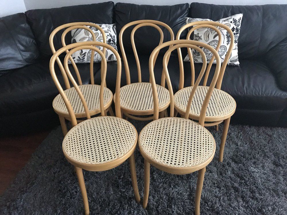 Four chairs are lined up on a sidewalk in front of a car