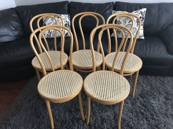 Four chairs are lined up on a sidewalk in front of a car