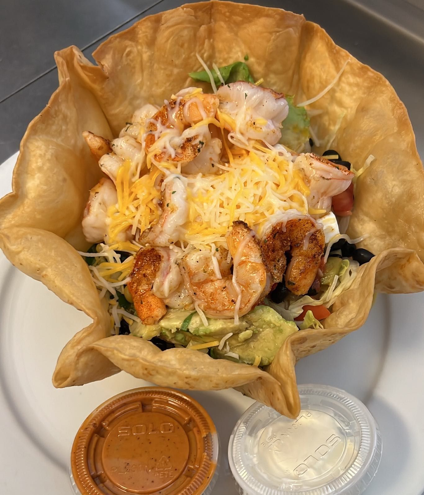 A taco salad with shrimp and cheese on a white plate
