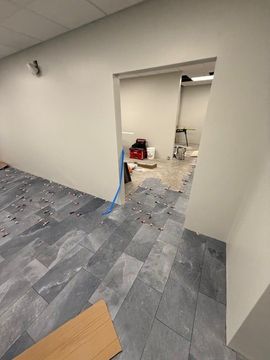 Empty office space with gray carpet, white walls, and a doorway leading to a room under renovation.