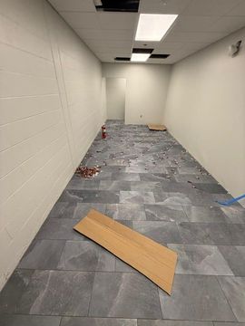 Empty hallway with gray tile floor, scattered debris, and a cardboard piece in the foreground.