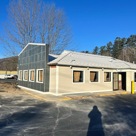 Small beige building with gray roof and black screened side wall under a clear blue sky