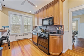 Bright kitchen with wood cabinets, black stove, and large windows over hardwood floors