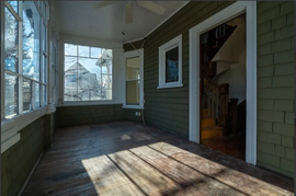 Enclosed porch with green siding, large windows, and sunlight on worn wooden floorboards
