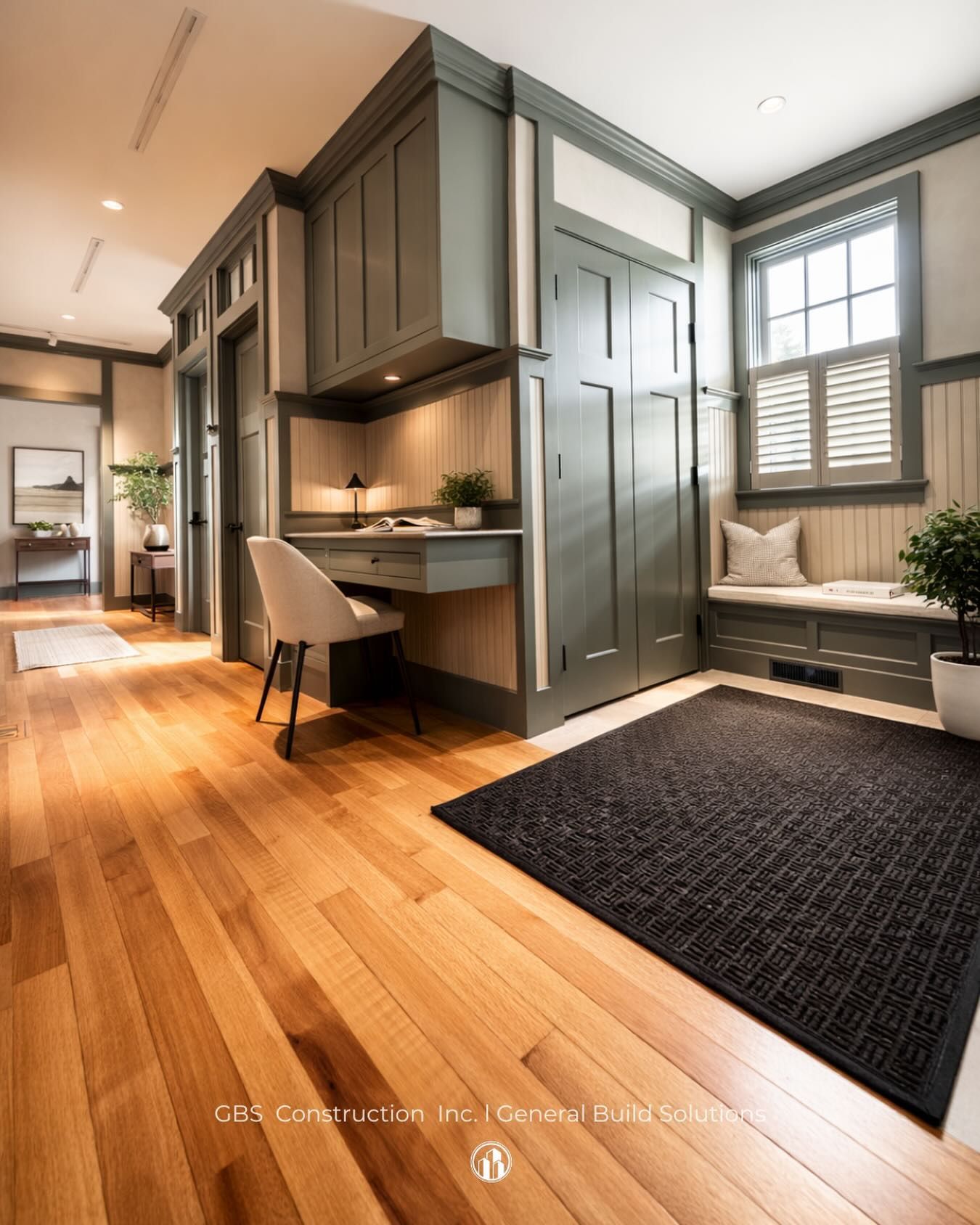 Modern studio interior with wood floors, gray built-ins, desk nook, window seat, and dark rug.