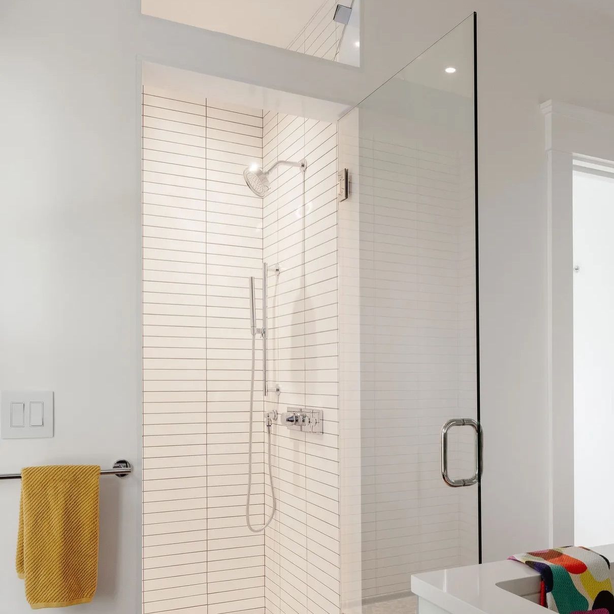 Modern white shower with glass enclosure, handheld showerhead, and yellow towel on a bathroom wall