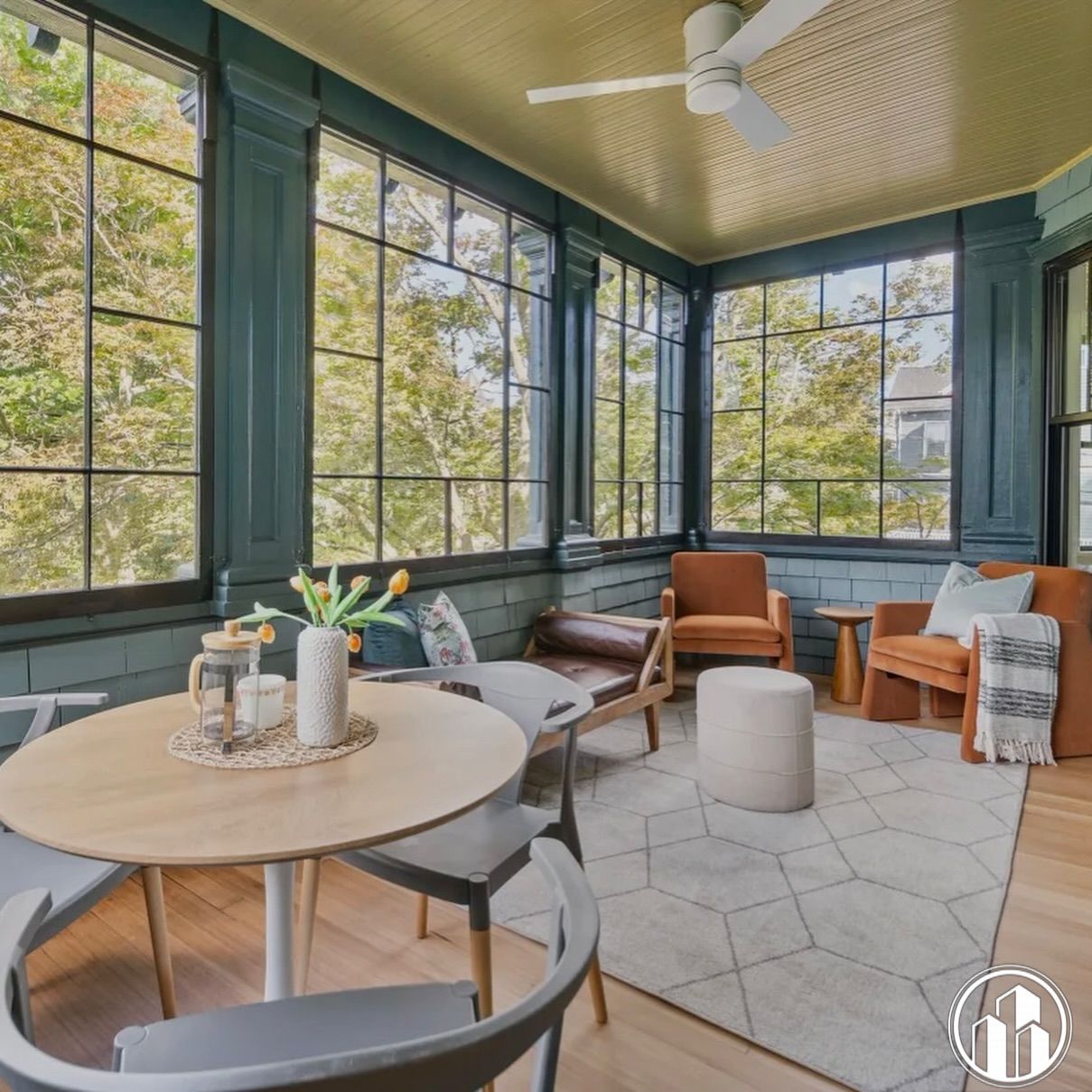 Bright sunroom porch with large windows, teal walls, round table, chairs, and orange accent seating