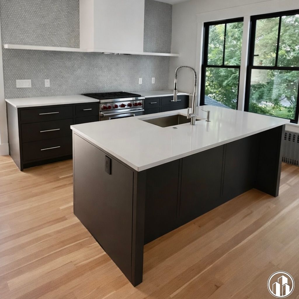Modern kitchen with dark cabinets, white island, stainless stove, and large windows overlooking greenery