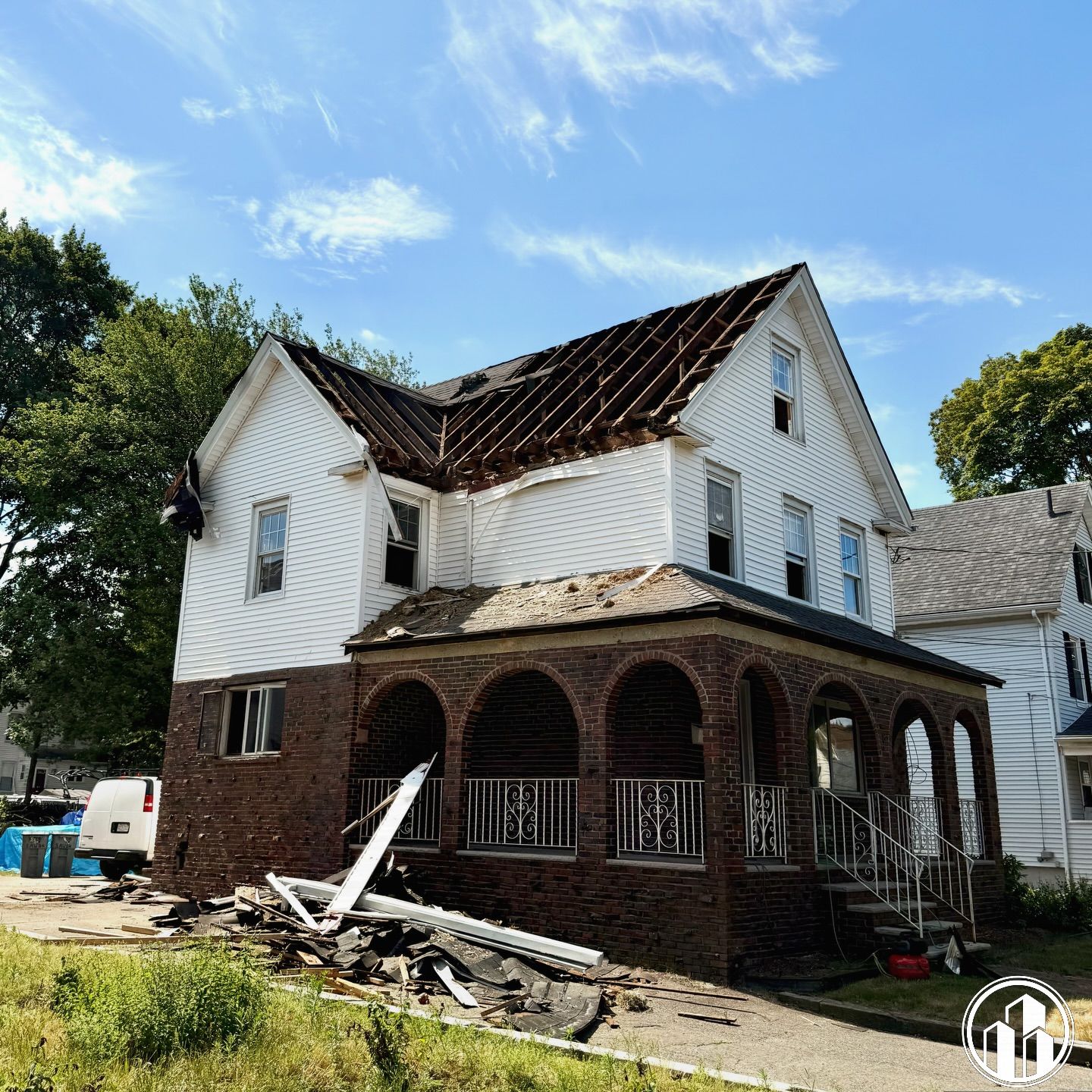 Damaged house with torn roof and debris after storm, white siding and brick porch under a blue sky