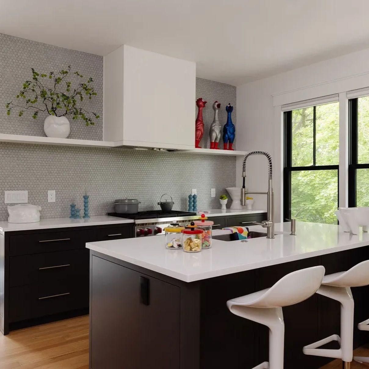 Modern kitchen with white island, black cabinets, open shelving, and large window overlooking greenery